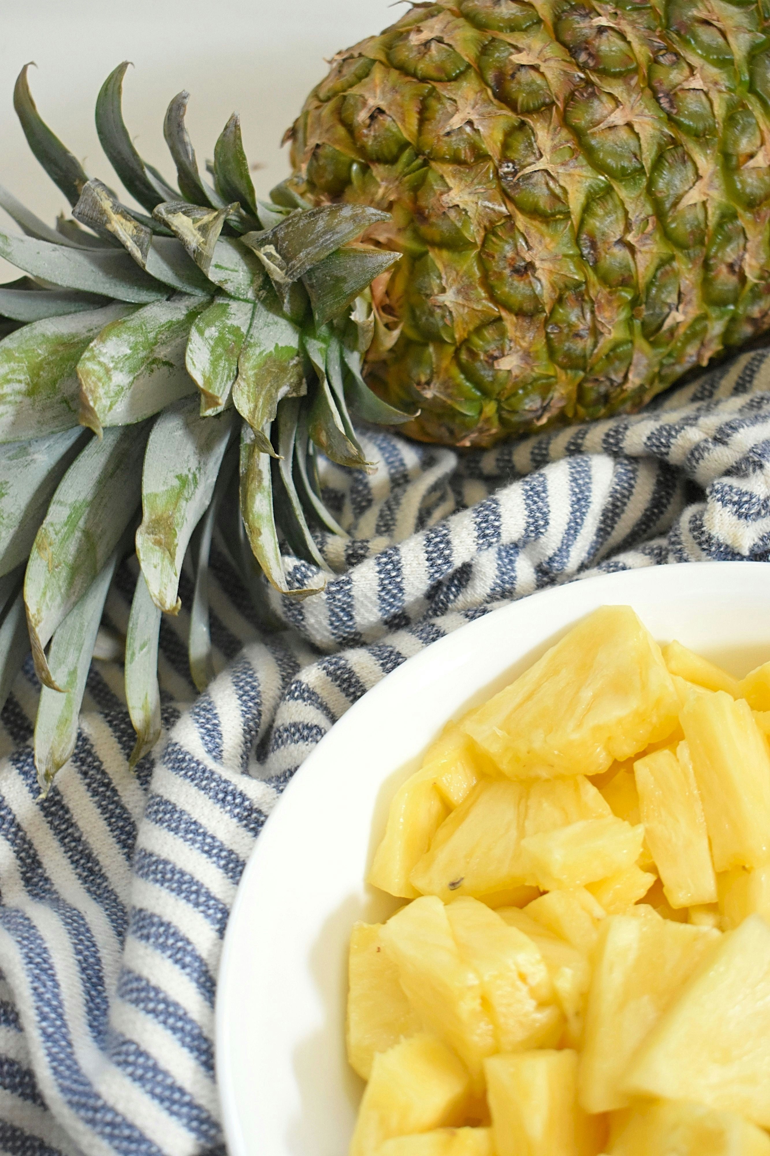 Whole pineapple and a bowl of pineapple chunks on a striped fabric background